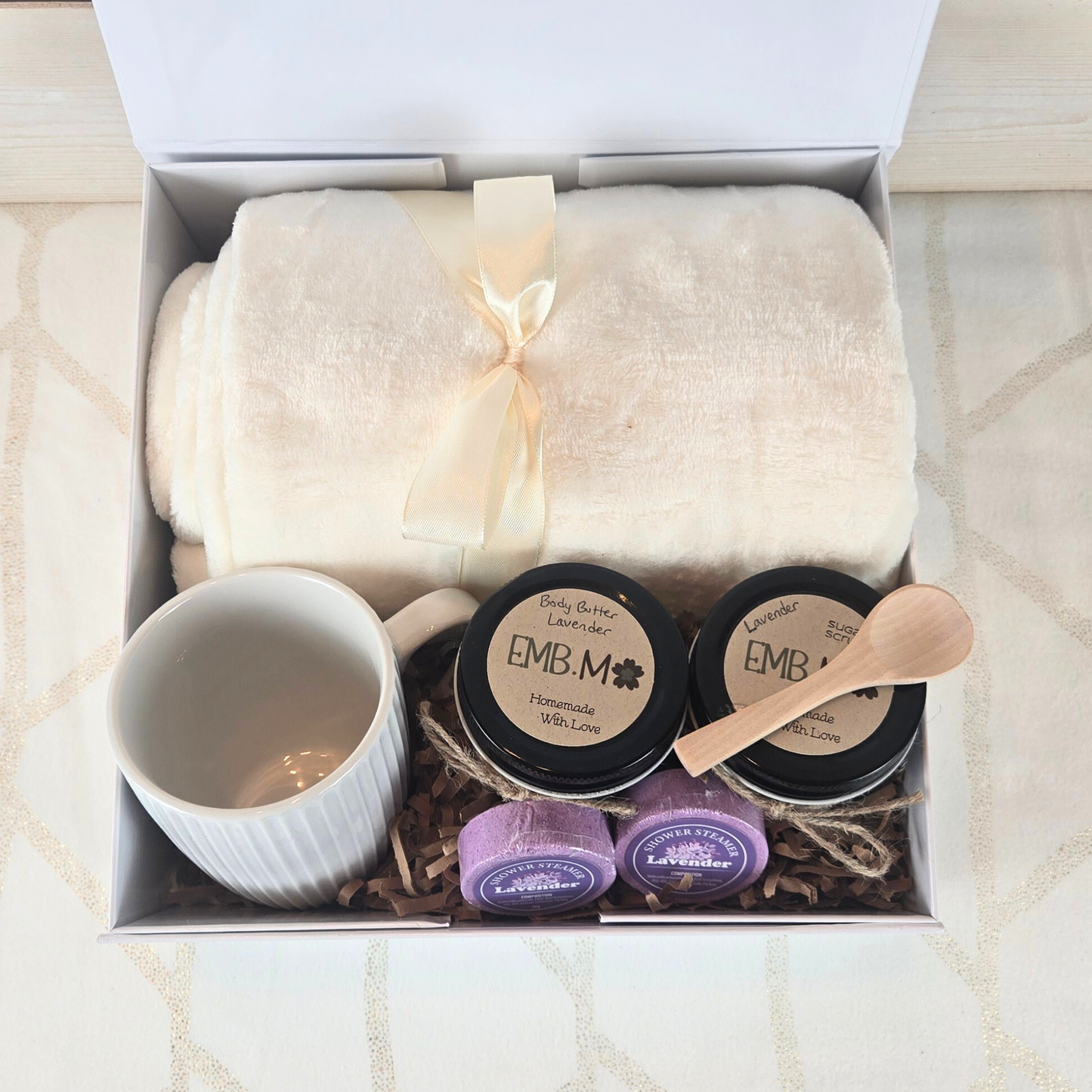 Ultimate pamper gift box for her. Includes a cozy blanket, luxurious body butter, invigorating sugar scrub, stylish mug, and refreshing shower steamers.