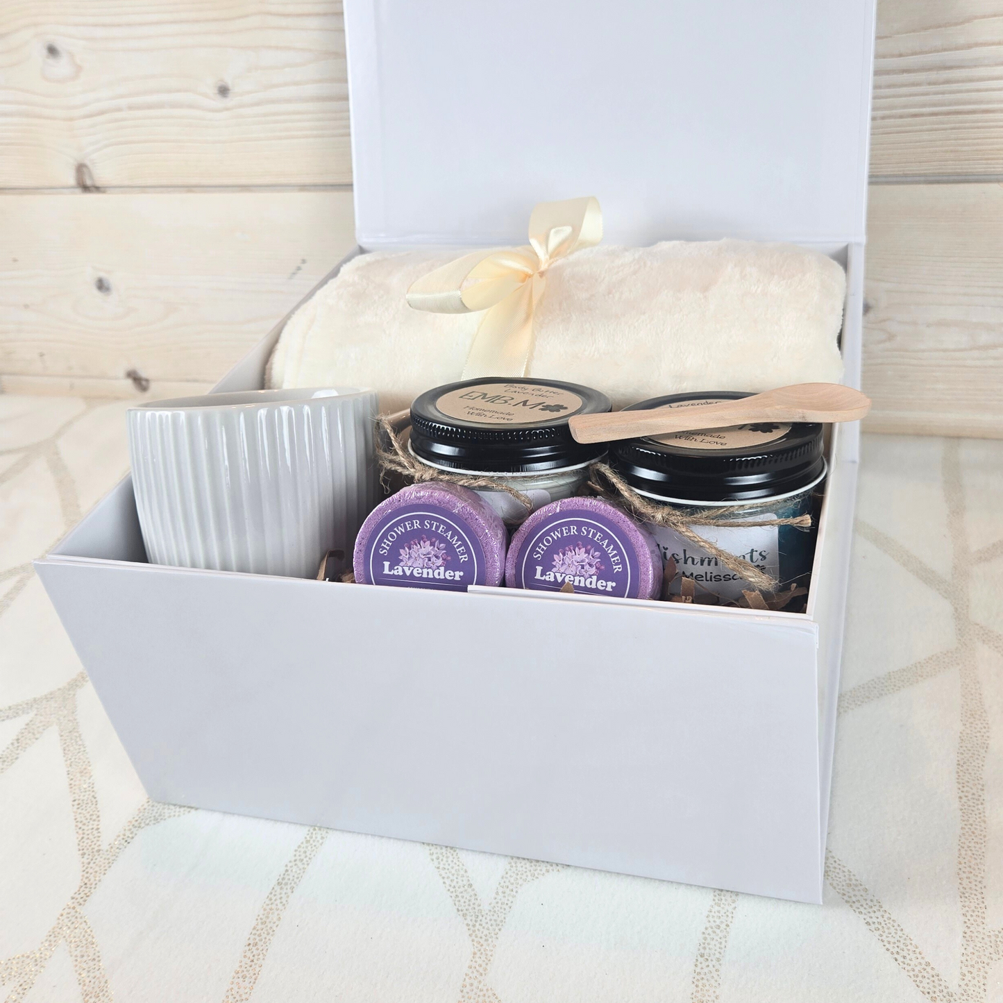 Ultimate pamper gift box for her. Includes a cozy blanket, luxurious body butter, invigorating sugar scrub, stylish mug, and refreshing shower steamers.