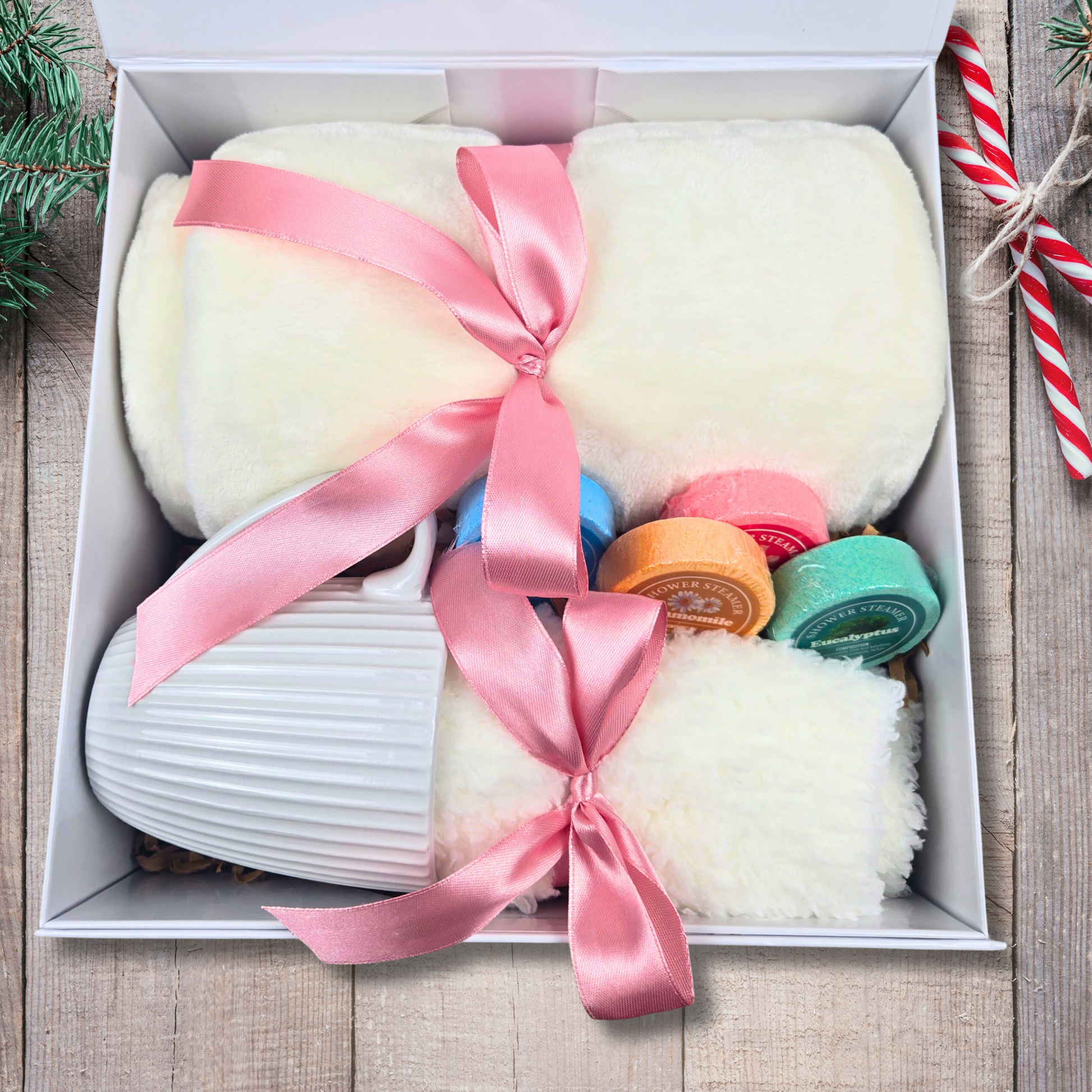 Thoughtfully curated gift box featuring a soft blanket, a stylish mug, fuzzy socks, and aromatic shower steamers for a cozy self-care treat.