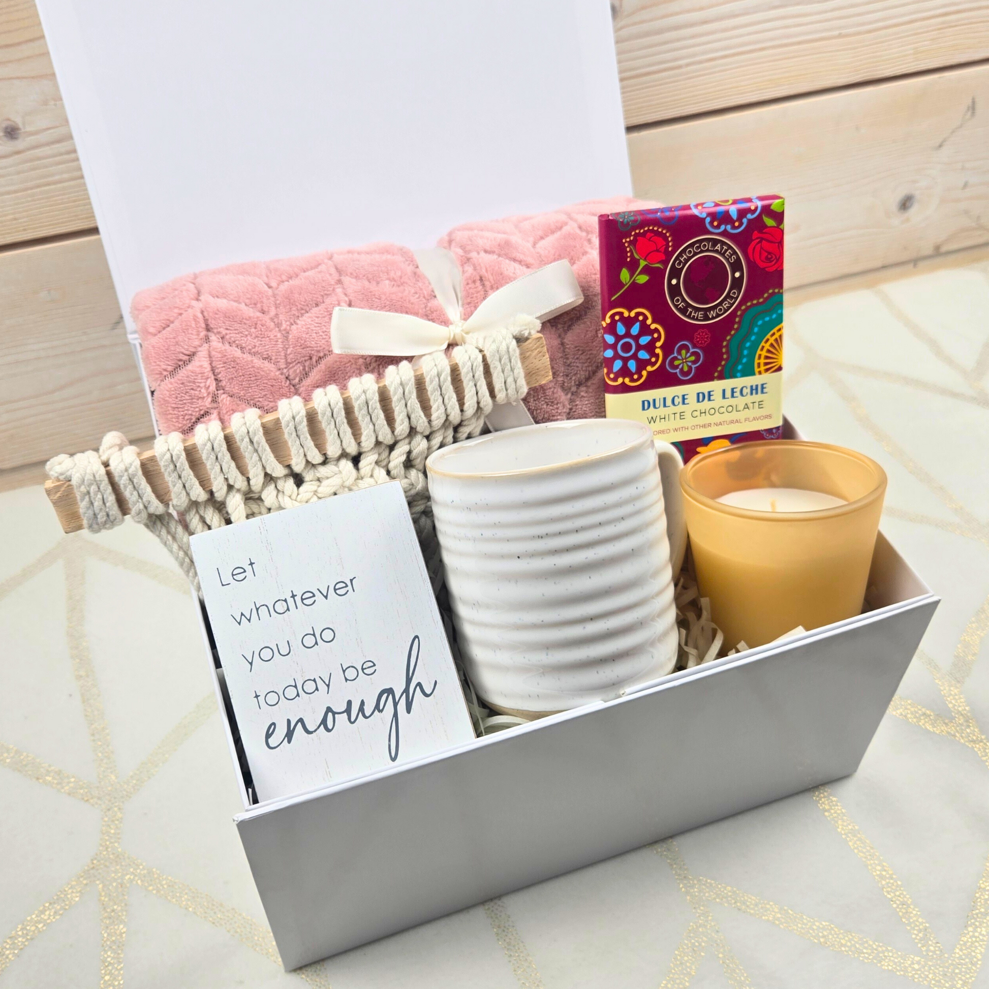 Encouragement gift for her including pink throw, wall decor, mug, vanilla-scented candle and dulce de leche white chocolate bar.