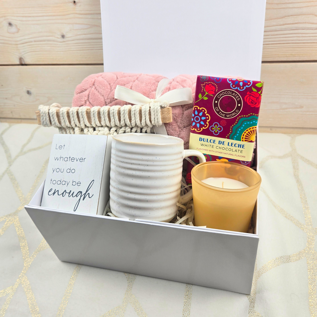 Encouragement gift for her including pink throw, wall decor, mug, vanilla-scented candle and dulce de leche white chocolate bar.