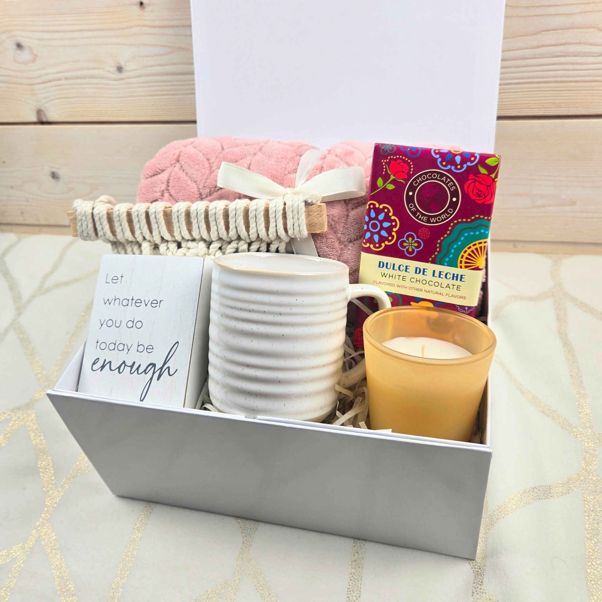 Encouragement gift for her including pink throw, wall decor, mug, vanilla-scented candle and dulce de leche white chocolate bar.