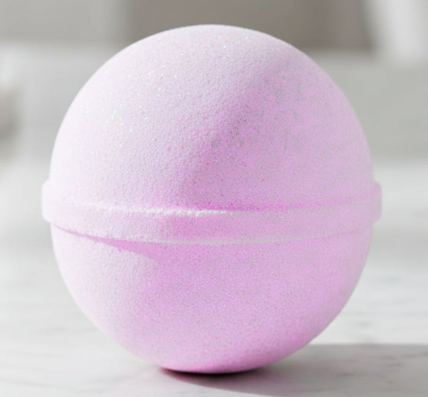 A round, light pink bath bomb, resting on a light marble surface.