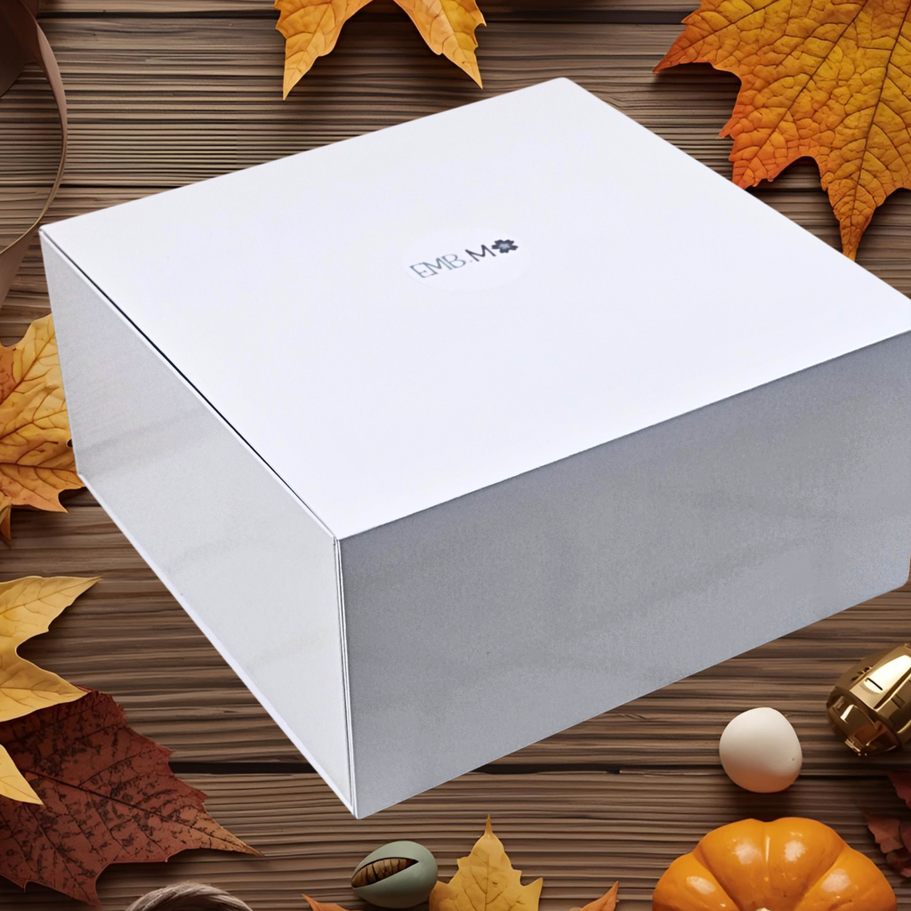 White gift box with a brand logo on a wooden surface with autumn leaves and small decorative items.