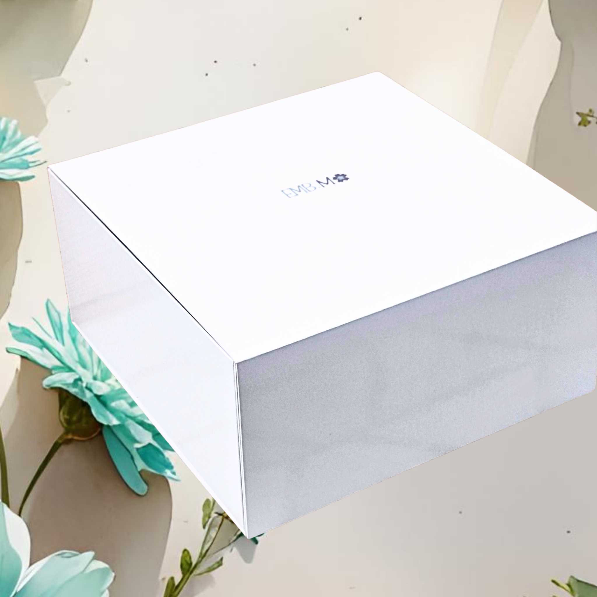 White rectangular box with a brand logo on a light surface with flowers.